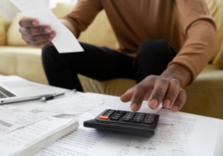 57% of over-55s struggling to clear mortgages before retirement  a man looks at a coffee table covered with receipts and a calculator