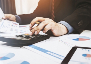 1 in 8 IFAs anticipate business downturn over the coming year man in business suit with calculator surrounded by graphs and paperwork