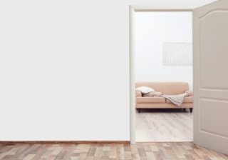 a wooden door in a white wall showing a living room through the gap