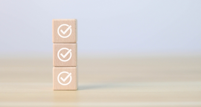 three wooden blocks with ticks on them, stacked in front of a blue background